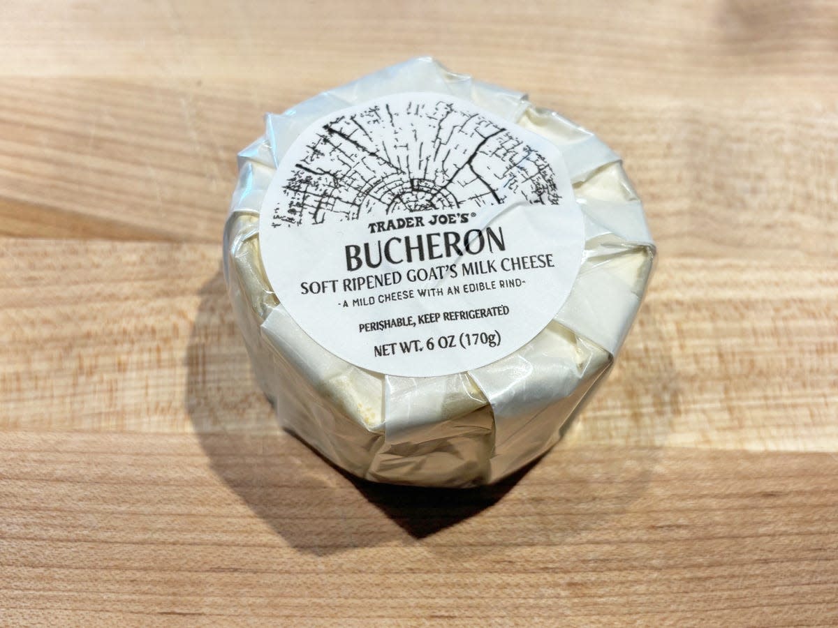 A circular cheese wrapped in white paper with a label reading "Trader Joe's Bucheron soft-ripened goat's milk cheese"