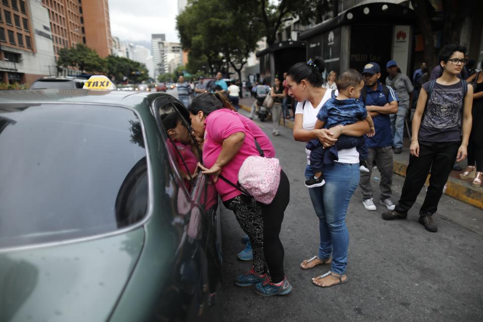 People ask a taxi driver how much it is to take them to their neighborhood during a blackout in Caracas, Venezuela, Monday, July 22, 2019. The lights went out across much of Venezuela Monday, reviving fears of the blackouts that plunged the country into chaos a few months ago as the government once again accused opponents of sabotaging the nation's hydroelectric power system. (AP Photo/Ariana Cubillos)