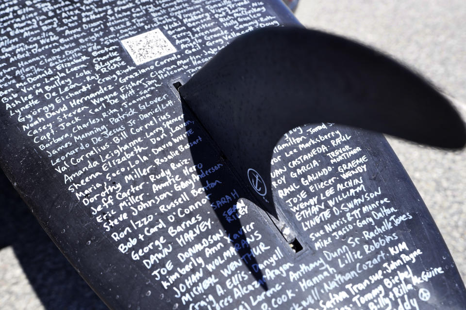 A surfboard belonging to Dan Fischer is covered with names of lost loved ones while resting on the ground at Easton's Beach, in Newport, R.I., Wednesday, May 18, 2022. Fischer, 42, created the One Last Wave Project in January 2022 to use the healing power of the ocean to help families coping with a loss, as it helped him following the death of his father. Fischer places names onto his surfboards, then takes the surfboards out into the ocean as a way to memorialize the loved ones in a place that was meaningful to them. (AP Photo/Steven Senne)