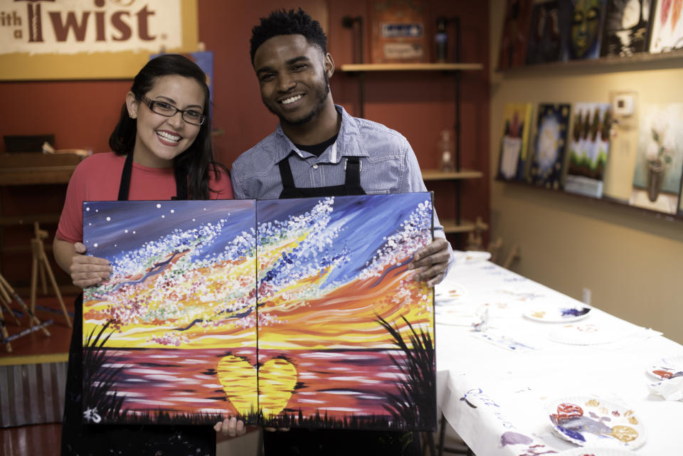 In this 2019 photo provided by Painting with a Twist, a couple reveals their date night art that when combined creates one piece of artwork they can display together, during a Painting with a Twist event in Mandeville, La. In recent years, the interactive painting industry has become a global sensation. Around the world, adults can spend their nights out learning to paint in a relaxed, BYOB setting. Thousands of franchises exist to help us all unleash our inner creative. (Painting with a Twist via AP)