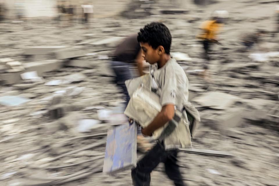 TOPSHOT - A child walks away with belongings salvaged from the rubble of a building hit in an Israeli strike on Rafah in the southern Gaza Strip on October 15, 2023. Israel embarked on a withering air campaign against Hamas militants in Gaza after they carried out a brutal attack on Israel on October 7 that left more than 1,400 people killed in Israel. (Photo by MOHAMMED ABED / AFP) (Photo by MOHAMMED ABED/AFP via Getty Images) ORG XMIT: 1537 ORIG FILE ID: AFP_33YD4NB.jpg