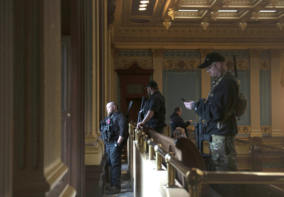 FILE - In this April 30, 2020, file photo, armed members of a militia group watch the protest outside while waiting for the Michigan Senate to vote at the Capitol in Lansing, Mich. In the past year, insurrectionists have breached the U.S. Capitol and protesters have forced their way into statehouses around the country. But the question of whether guns should be allowed in capitol buildings remains political and states are going in opposite directions. (Nicole Hester/MLive.com/Ann Arbor News via AP File