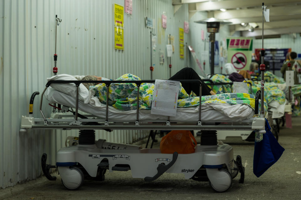 A row of three patients lie in beds in a hospital setting.