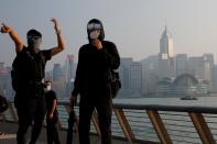 Masked anti-government protesters react in front of the skyline during a protest at Tsim Sha Tsui in Hong Kong