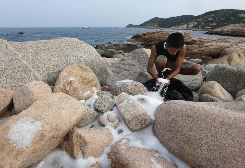 A volunteer collects plastic pellets washed up on a bank of Lamma island during a cleanup operation in Hong Kong Sunday, Aug. 5, 2012. Hong Kong government said about 150 tons of the pellets were spilled into the sea from a vessel when Typhoon Vicente hit two weeks ago, and some of the pellets drifted into fish farms. (AP Photo/Kin Cheung)