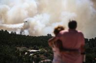 <p>A couple watches an helicopter dropping water on a wildfire near Monchique, in Algarve, on Aug. 8, 2018. Spain and Portugal approached record temperatures at the weekend, with the mercury hitting 46.6 degrees Celsius (116 Fahrenheit) at El Granado in Spain and 46.4 C in Alvega, Portugal, according to the World Meteorological Organisation (WMO). While the deadly hot spell is expected to ease in parts of western Europe in the coming days, firefighters in Spain and Portugal struggled to contain wildfires that have swept southern areas. (Photo: Carlos Costa/AFP/Getty Images) </p>