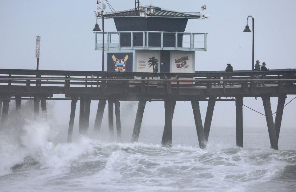 People stand on a pier over the Pacific Ocean with Tropical Storm Hilary approaching in San Diego County on Sunday.