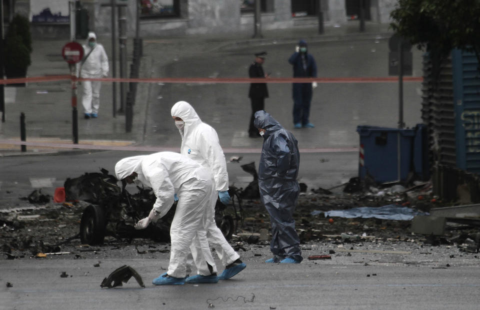 Police bomb disposal experts search for evidence next to remains of a car after a car bomb explosion in central Athens on Thursday, April 10, 2014. A bomb exploded outside a Bank of Greece building in central Athens before dawn Thursday, causing some damage but no injuries. The blast came hours before Greece was to return to the international bond markets for the first time in four years, and a day before German Chancellor Angela Merkel was to visit Athens.(AP Photo/Dimitri Messinis)