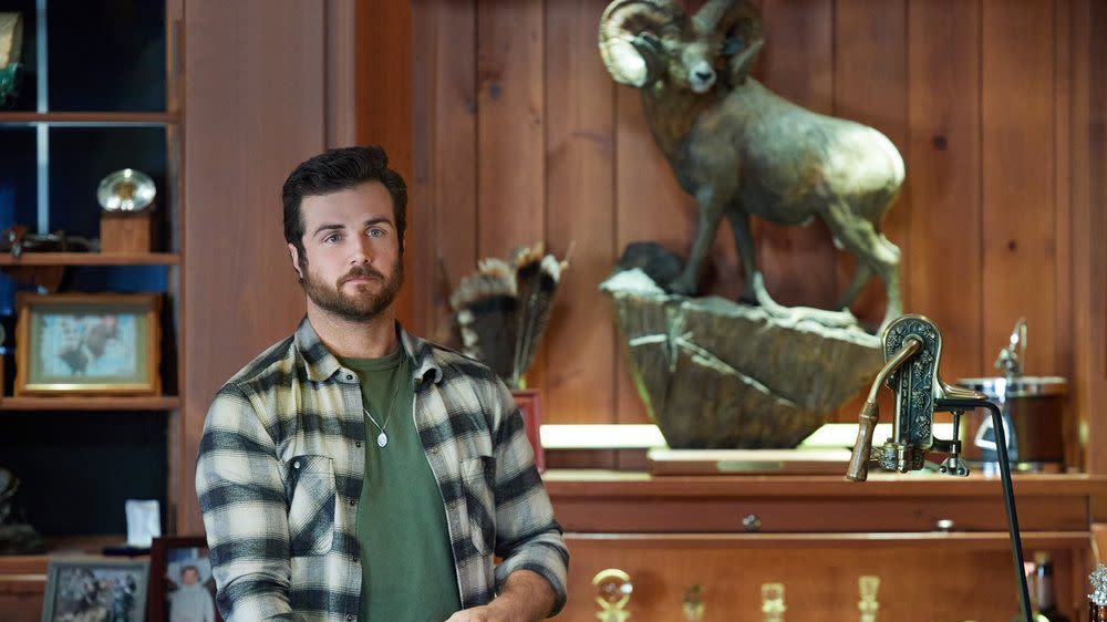 a man standing in front of a shelf with trophies and a statue