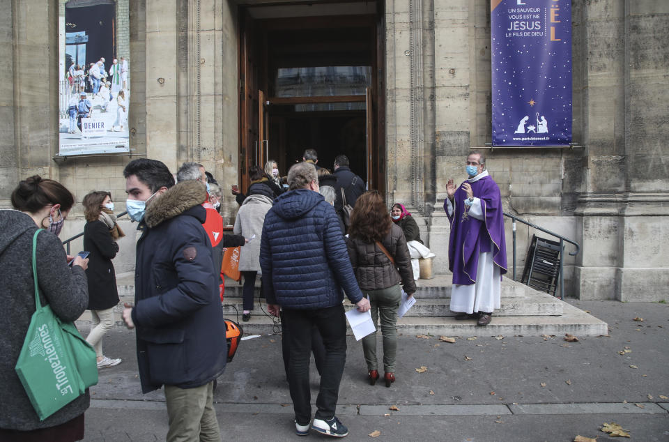 Priest Antoine d'Eudeville, right, wearing a face mask as a precaution against the coronavirus welcomes church-goers as they lineup at the entrance of the Notre-Dame-des-Champs church in Paris, Sunday, Nov. 29, 2020. French churches, mosques and synagogues can open their doors again to worshippers - but only a few of them, as France cautiously starts reopening after a second virus lockdown. Some churches may defy the 30-person limit they feel as too unreasonable, and other sites may stay closed until they can reopen for real. (AP Photo/Michel Euler)