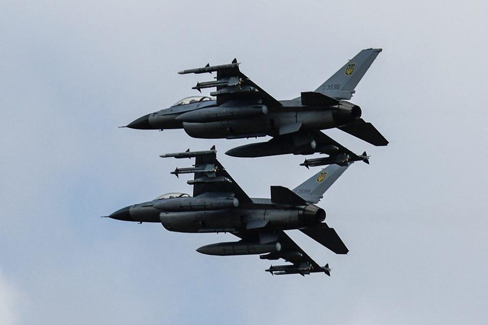 Two F-16 fighter jets fly side by side against the blue sky.