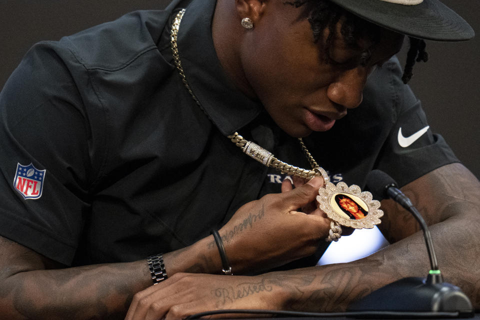 Baltimore Ravens first round draft pick Zay Flowers looks at a pendant sporting a photograph of his mother Jackie Walden with petals with the initials of his 13 siblings as he participates in a news conference at the NFL football team's training center in Owings Mills, Md., Friday, April 28, 2023. Walden died from a head injury when Flowers was five years old. (AP Photo/Julio Cortez)