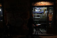 A bartender carries a table inside as he is closing the Nilo Bar in Naples, in the region of Campania, Italy, Friday, Nov. 13, 2020. The regions of Campania and Tuscany were designated red zone on Friday, signaling the dire condition of a hospitals struggling with a surge of new admissions. (AP Photo/Gregorio Borgia)