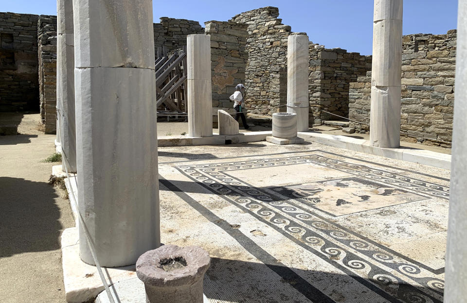 In this Tuesday, June 9, 2020 photo an Archaeological Service worker walks past marble columns on the island of Delos, an ancient center of religious and commercial life, in Greece. The site is open for day trips for visitors on vacation on the nearby island of Mykonos. Business owners and locals officials on the Greek holiday island of Mykonos, a popular vacation spot for celebrities, club-goers, and high rollers, say they are keen to reopen for business despite the risks of COVID-19 posed by international travel. Greece will official launch its tourism season Monday, June 15, 2020 after keeping the country's infection rate low. (AP Photo/Derek Gatopoulos)