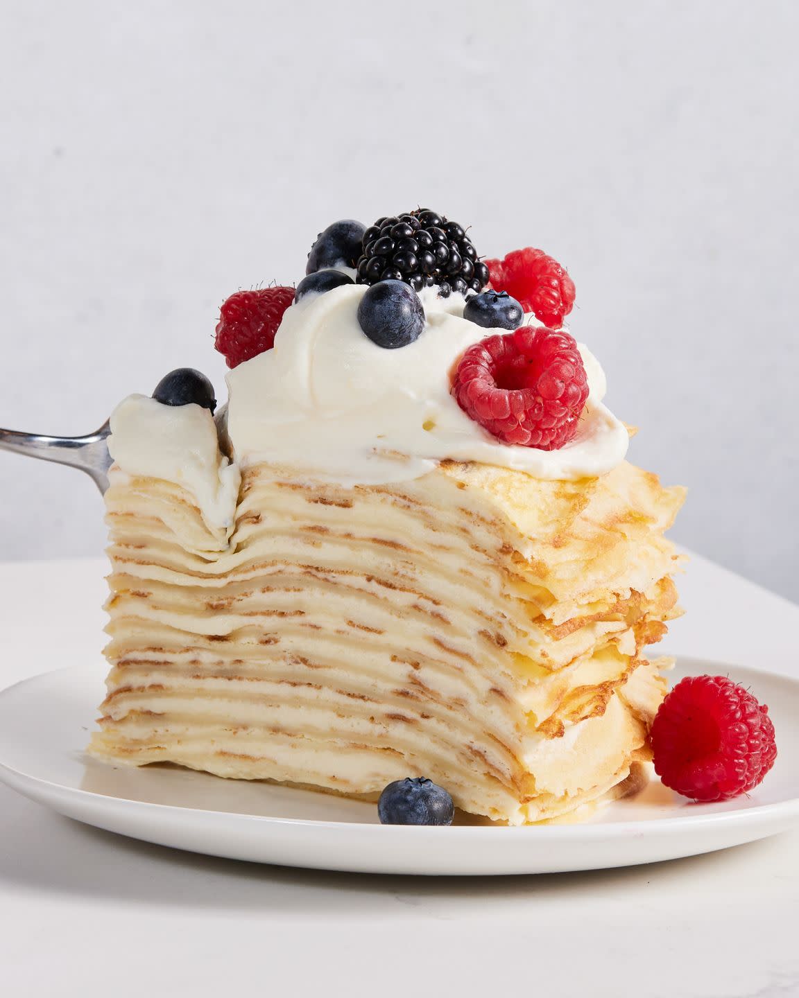 slice of crepe cake on a plate topped with whipped cream and mixed berries