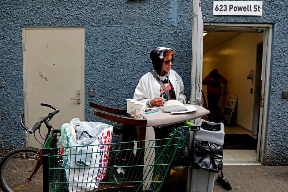 A woman with a bicycle and shopping cart outside a building