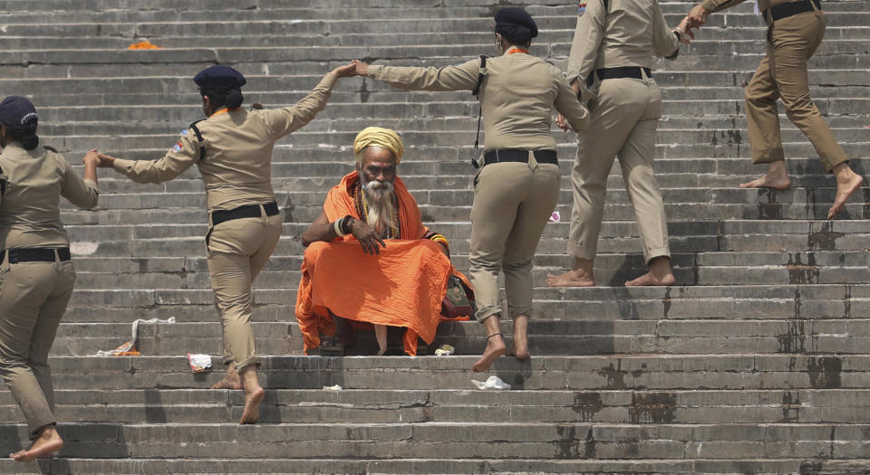 Police women clear a ghat as a Hindu holy man sits during Kumbh Mela, or pitcher festival, one of the most sacred pilgrimages in Hinduism, in Haridwar, northern state of Uttarakhand, India, Monday, April 12, 2021. Tens of thousands of Hindu devotees gathered by the Ganges River for special prayers Monday, many of them flouting social distancing practices as the coronavirus spreads in India with record speed. (AP Photo/Karma Sonam)
