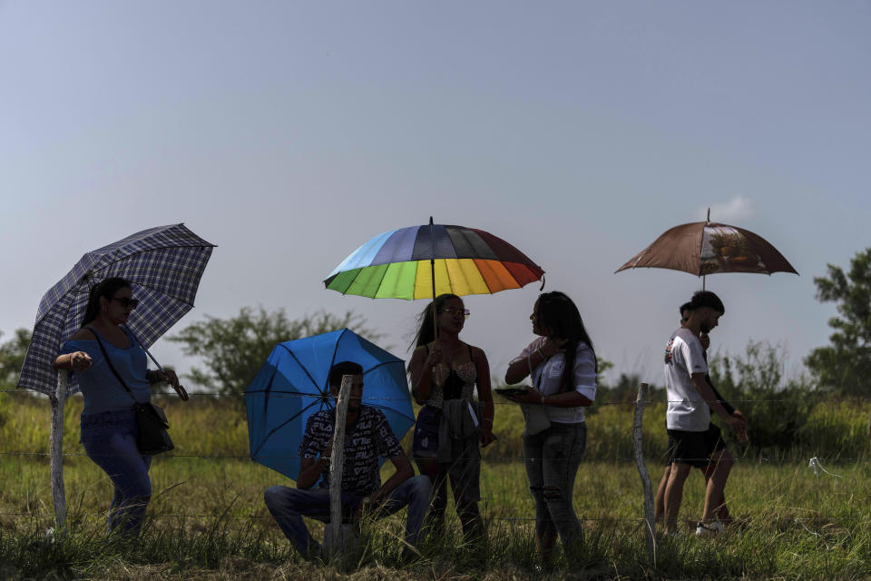 Los espectadores se protegen con sombrillas mientras esperan el inicio de las carreras de resistencia en una antigua pista de aterrizaje en desuso en San Nicolás de Bari, Cuba, el domingo 23 de julio de 2023. (Foto AP/Ramón Espinosa)