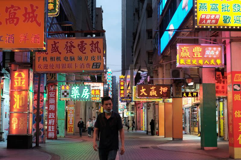 A man walks near casinos, past shops with neon lights on, in Macau