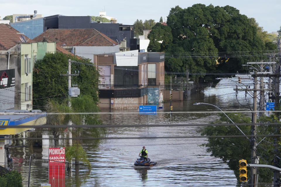 A man rides a jet ski on a flooded street after heavy rain in Porto Alegre, Rio Grande do Sul state, Brazil, Thursday, May 9, 2024. (AP Photo/Andre Penner)