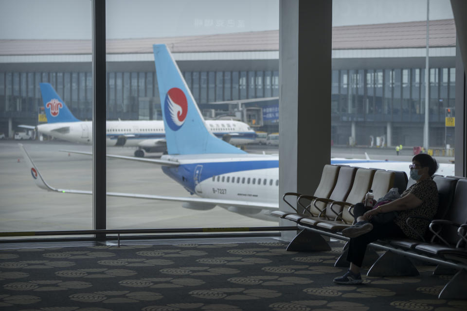 A traveler wearing a face mask sits near a parked jetliner from Hebei Airlines at Beijing Daxing International Airport in Beijing, Sunday, May 28, 2023. China's first domestically made passenger jet flew its maiden commercial flight on Sunday, as China looks to compete with industry giants such as Boeing and Airbus in the global aircraft market. (AP Photo/Mark Schiefelbein)