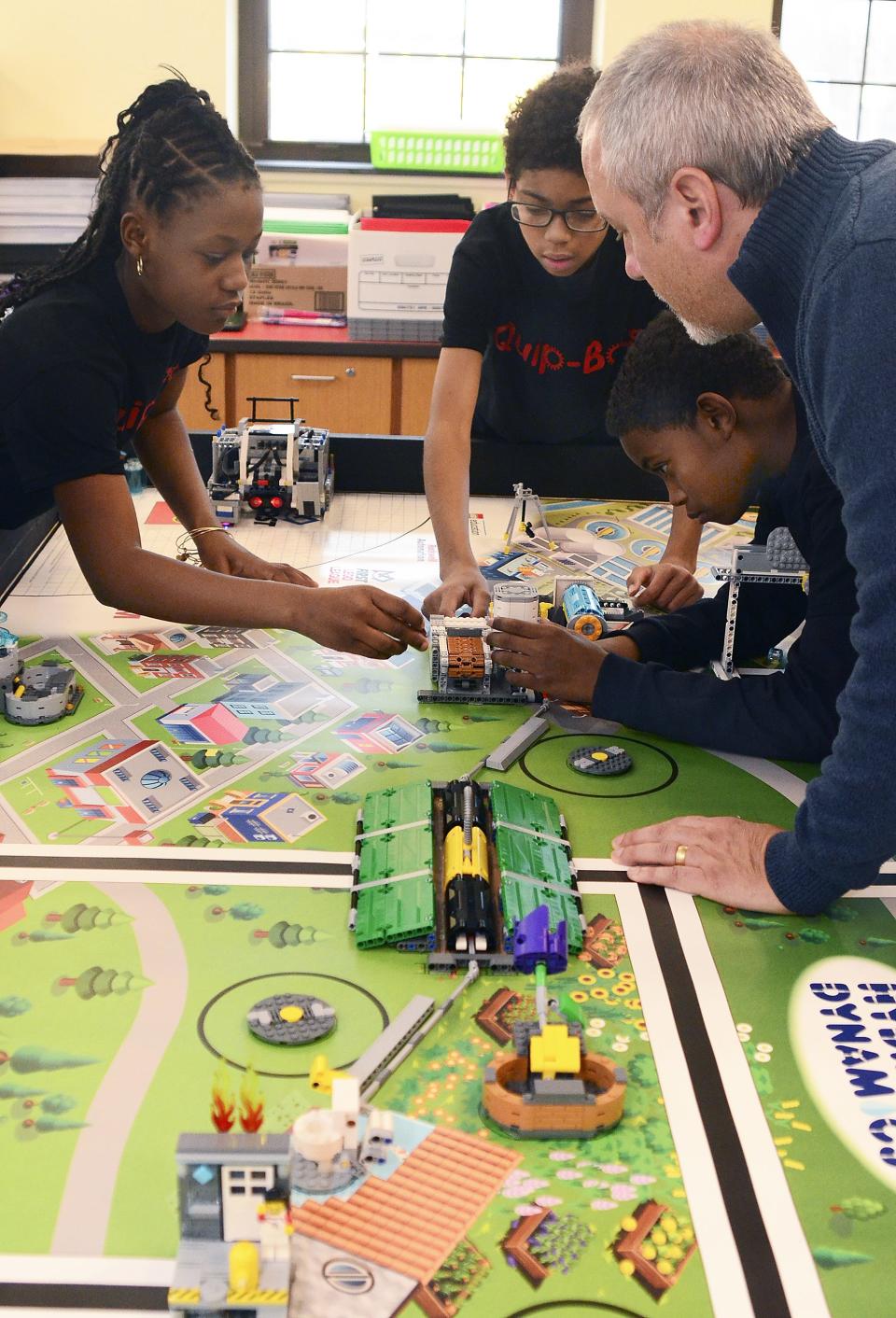 File photo of Aliquippa Elementary School science teacher Robert Signorelli, right, watching as members of the Quip-Bots practice a skill with a robot they built with Legos. From left are Jahnauri Riggins, Richard McCracken and his brother, Jasir McCracken. [BCT file]