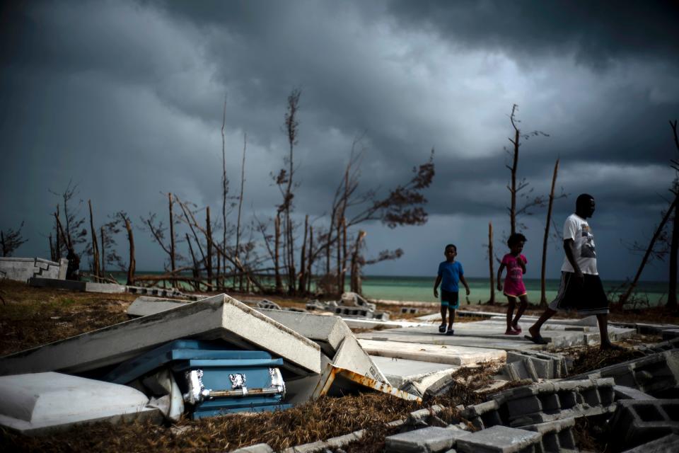 People walk next to a shattered and water-filled coffin lays exposed to the elements in the aftermath of Hurricane Dorian, at the cemetery in Mclean's Town, Grand Bahama, Bahamas, Friday Sept. 13, 2019.