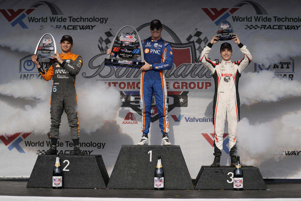 Scott Dixon holds the first place trophy on the podium alongside second place finisher Pato O'Ward, left, and third place finisher David Malukas, right, following an IndyCar auto race at World Wide Technology Raceway, Sunday, Aug. 27, 2023, in Madison, Ill. (AP Photo/Jeff Roberson)