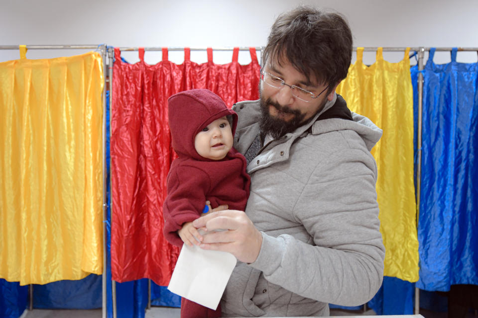 A man holds a baby as he prepares to cast his vote in Bucharest, Romania, Sunday, Nov. 24, 2019. Romanians are voting in a presidential runoff election in which incumbent Klaus Iohannis is vying for a second term, facing Social Democratic Party leader Viorica Dancila, a former prime minister, in Sunday's vote. (AP Photo/Andreea Alexandru)