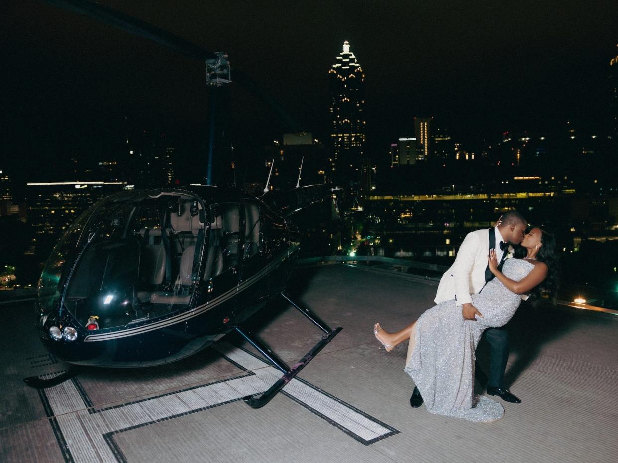 A bride and groom kiss next to a helicopter.