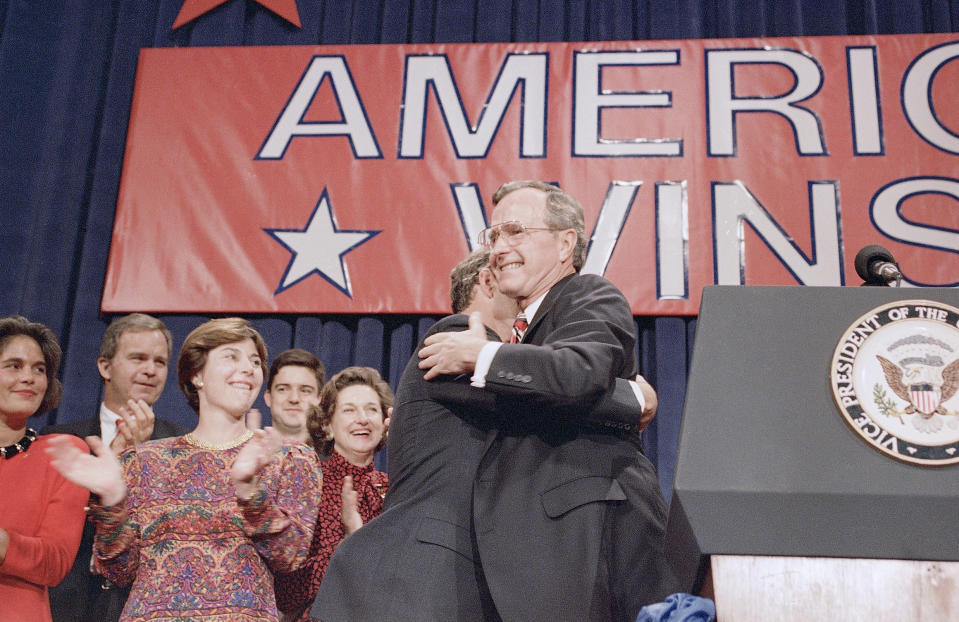 FILE - In this Nov. 8, 1988 file photo, President-elect George H. W. Bush, right, hugs his son George W. Bush, center left, during his victory rally, in Houston, Texas. Other Bush family members are from left: Columba Bush, Jeb Bush, and Laura Bush. Presidents George H.W. Bush and George W. Bush were both conservatives, but during very different times. The elder Bush was a Republican who could carve an occasional moderate path without a crushing response from the right. His was an era of stepping back from the prospect of doomsday, with the collapse of the Soviet Union, and a far more limited threat emerging with Iraq’s invasion of Kuwait. But that was not at all like the Sept. 11 terrorist attacks that came early to his son. (AP Photo, File)