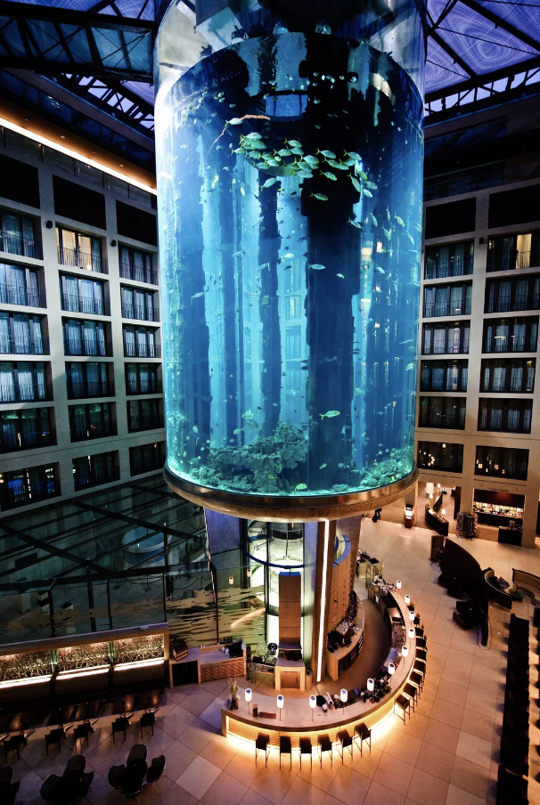 Giant cylindrical aquarium spanning several floors in a building's atrium, surrounded by balconies and seating areas