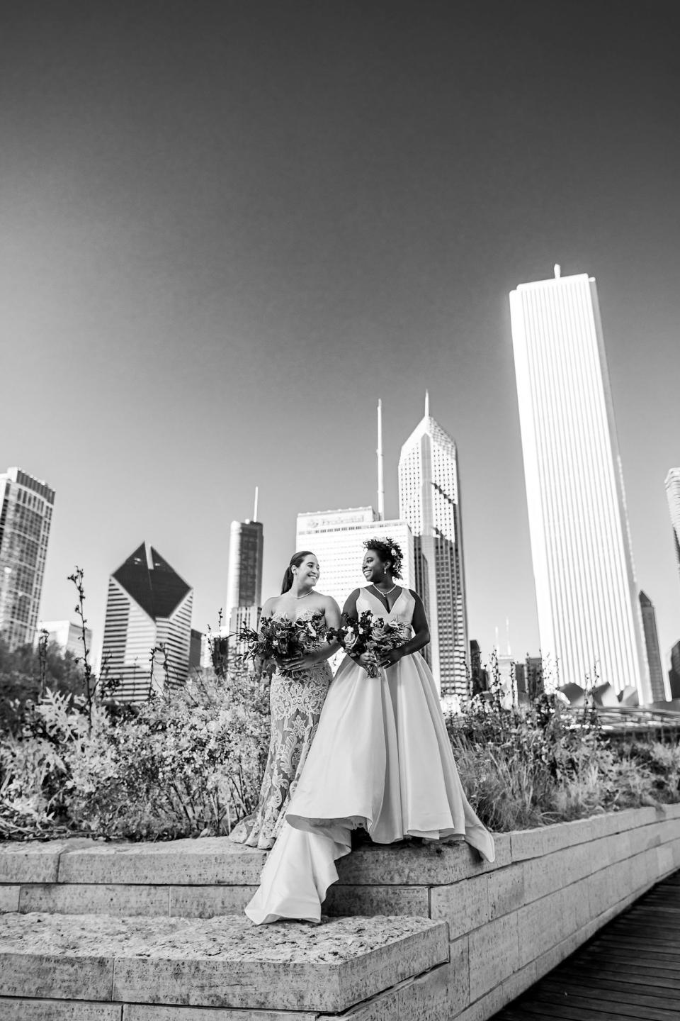 A black and white photo of two brides looking at each other in front of a cityscape.