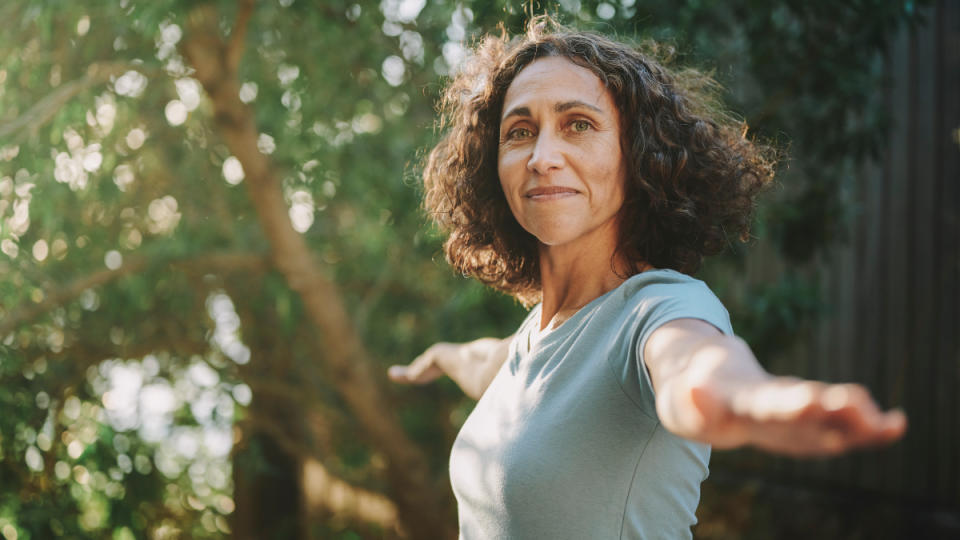 A woman with dark hair holding a yoga pose with her arms out, which is a physical exercise that can help with restless leg syndrome