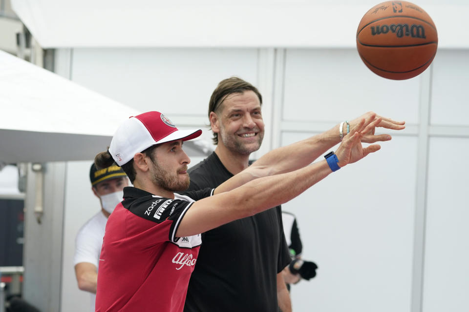 Alfa Romeo driver Antonio Giovinazzi, of Italy, left, is helped by former NBA player Fabricio Oberto, right, as he shoots free throws at the Formula One U.S. Grand Prix auto race at the Circuit of the Americas, Thursday, Oct. 21, 2021, in Austin, Texas. F1 Teams took part in a free throw challenge as to help the NBA celebrate their 75th Anniversary. (AP Photo/Eric Gay)