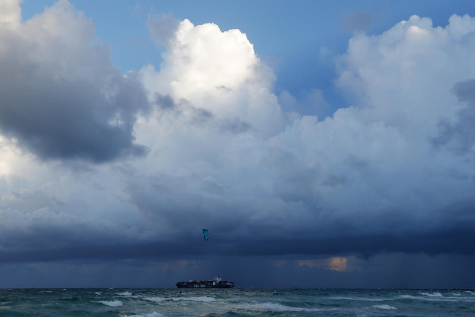 A container ship heads out to sea into bands of rain as a kitesurfer enjoys the winds off South Beach, Friday, Aug. 30, 2019, on Miami Beach, Fla. All of Florida is under a state of emergency and authorities are urging residents to stockpile a week's worth of food and supplies as Hurricane Dorian gathers strength and aims to slam the state as soon as Monday as a Category 4 storm. (AP Photo/Wilfredo Lee)