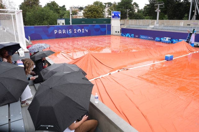 Spectators sit under umbrellas on an outside court