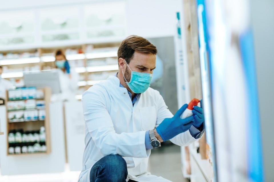 Male pharmacist with protective mask and face shield on his face, working at pharmacy.