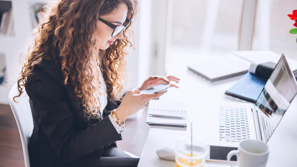 Stylish woman working in her modern office, using laptop, mobile phone, taking notes and searching the internet.