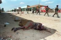 Rwandan Patriotic Front (RPF) soldiers walking past the corpse of a woman killed by the pro-government militia in Kayove, Rwanda, in June, 1994