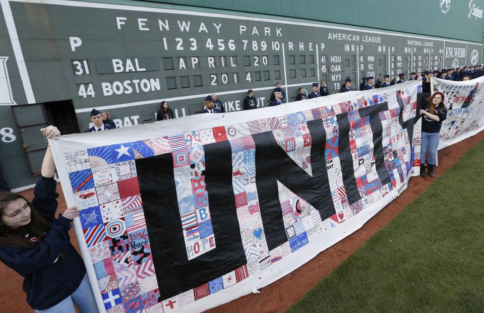 People hold banners in front of the scoreboard at Fenway Park during ceremonies to commemorate the one-year anniversary of the Boston Marathon bombings before a baseball game between the Boston Red Sox and the Baltimore Orioles in Boston, Sunday, April 20, 2014. (AP Photo/Michael Dwyer)