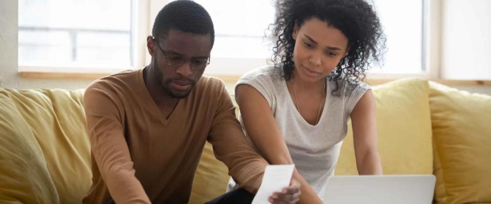 Serious african american couple using calculator and laptop for calaulating finance. Diverse upset man and woman taxing, accounting with check credit analytic for mortgage payment.