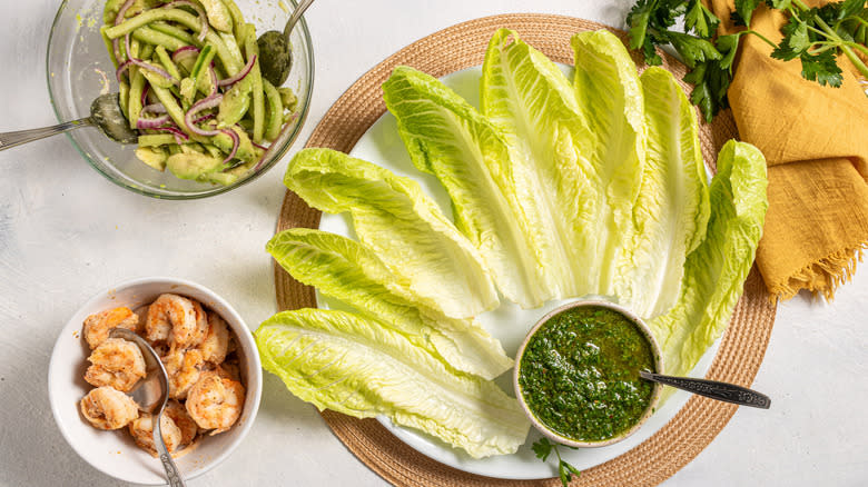 Romain lettuce leaves on a plate with green sauce and sides of shrimp and cucumber salad