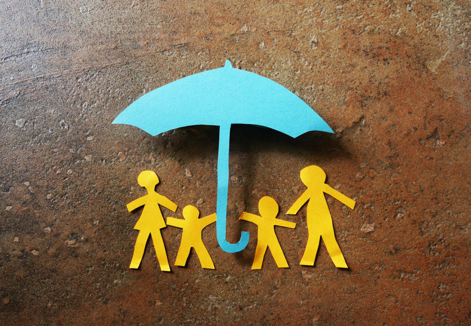 Paper family of four under a paper cutout umbrella