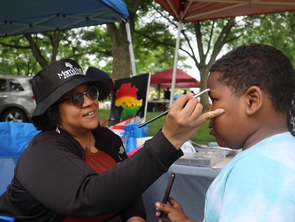 Monique Livingston paints the face of 9-year-old Khalid Gasque at a booth for her home business, Mama Root, at Utica's Juneteenth Celebration Saturday, June 18, 2022 at Chancellor Park.
