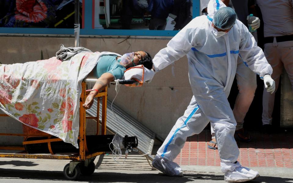 A health worker wearing personal protective equipment pulls the bed of a patient suffering from Covid-19 outside the casualty ward at Guru Teg Bahadur hospital in New Delhi -  ADNAN ABIDI / REUTERS