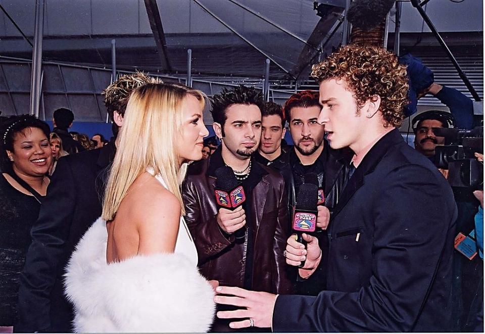 Spears smiling as Timberlake interviews her and puts his hand out toward her