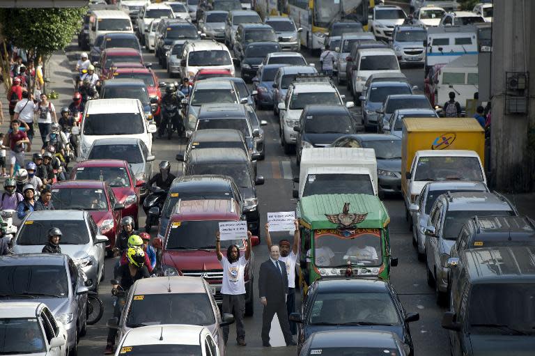 Greenpeace members hold a banner near a life size picture of French President Francois Hollande (C) and an electric jeep powered by 100% renewable energy in the middle of a traffic jam in Manila on February 25, 2015