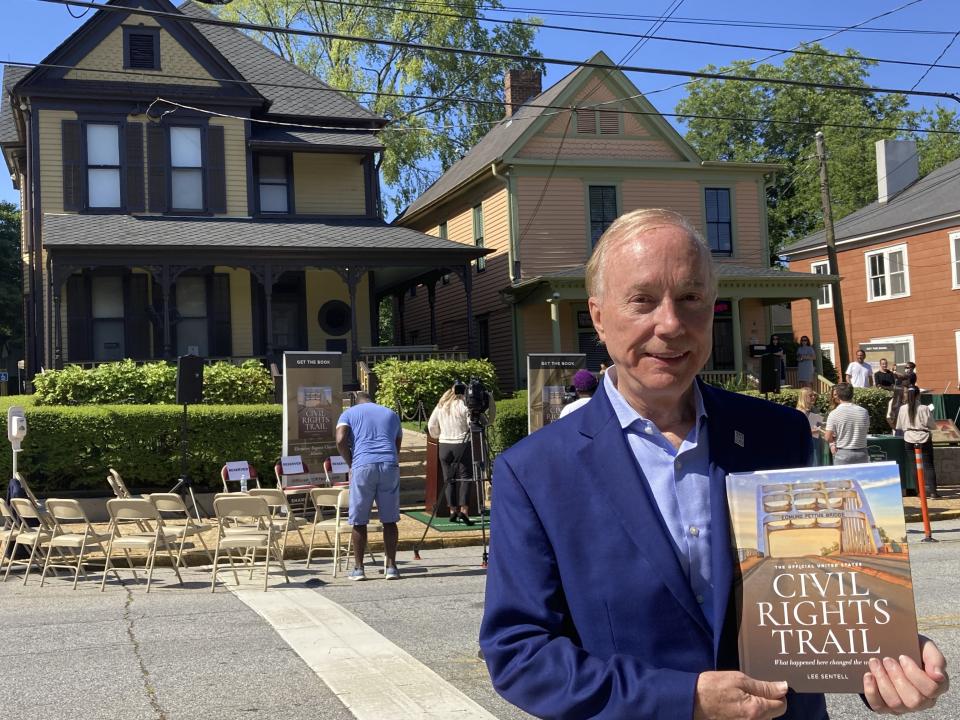 Lee Sentell, author of “The Official United States Civil Rights Trail” companion book, poses with the book outside the birth home of the Rev. Martin Luther King Jr. in Atlanta on Wednesday, June 23, 2021. The U.S. Civil Rights Trail includes more than 120 sites — churches, schools, courthouses, museums — across 15 states, mostly in the South. The new companion book includes more than 200 images of those landmarks today, as well as photographs from the civil rights era. (AP Photo/Kate Brumback)