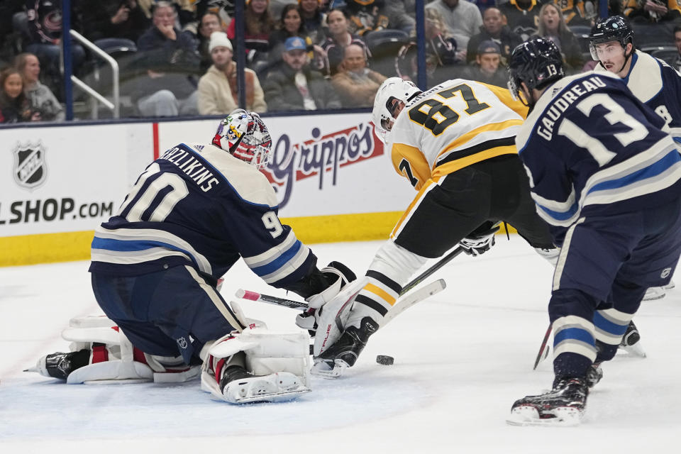 Pittsburgh Penguins center Sidney Crosby (87) and Columbus Blue Jackets goaltender Elvis Merzlikins (90) reach for the puck during the first period of an NHL hockey game Tuesday, Nov. 14, 2023, in Columbus, Ohio. (AP Photo/Sue Ogrocki)